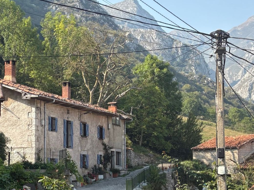 A stone village house with terracotta roof tiles below a limestone mountain, the kind of reference photo you would paint from.